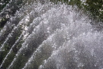 Splashes of water on dark background. Water sprays in sunny day close-up.