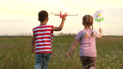 Little boy and girl play with toy plane and windmill walking on large meadow