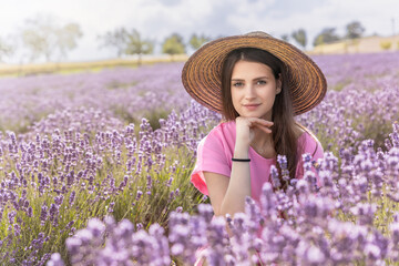 Portrait of beautiful tanned girl in straw hat posing supports her chin in purple lavender field.  Horizontally. 