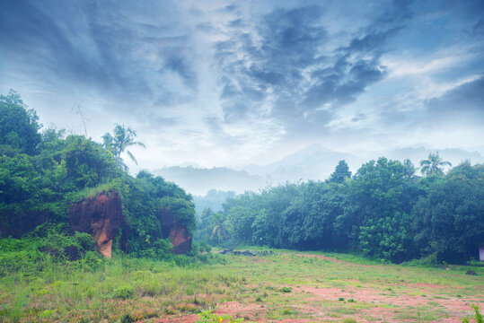 Landscape photography- A hillside full of green under a cloudy sky. In the distance, you can see breathtaking mountains
