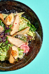 Caesar salad with chicken and cheese in a plate on a blue background