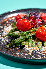 Salad with baked asparagus and tomatoes in a plate on a blue background
