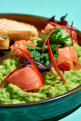 Avocado guacamole with salted salmon in a plate with toasted bread on a blue background