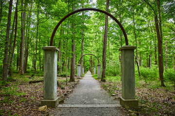 Lush green forest surrounding row of arches along woodland path through park