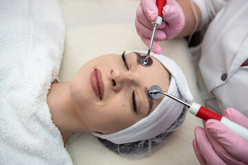 beautician performing microcurrent stimulation young woman on face at spa clinic