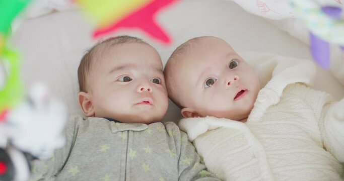 Cute little twins boy and girl lie in bed. Two caucasian babies brother and sister lying together look at the newborn toy in the bedroom at home. Happy family childhood, kid bedtime lifestyle.