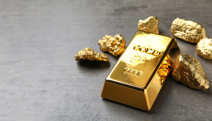 Gold ingots and nuggets on grey table. Space for text