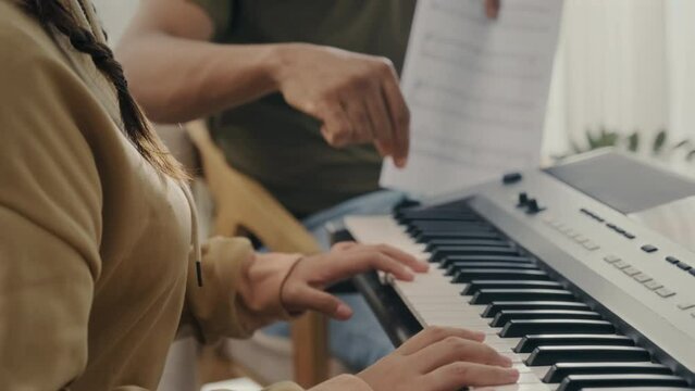 Music teacher explaining teenagers student with music notes where to put fingers on synthesizer during private lesson