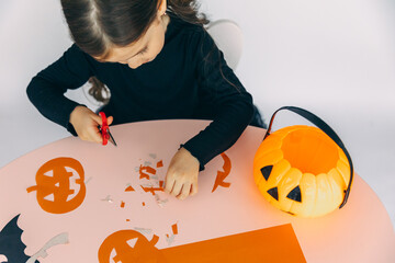 Happy laughing child girl in a witches costume preparing for Halloween and decorating the house. Child cut a pumpkin for Halloween holiday. Top view