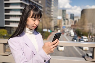 Fototapeta na wymiar A portrait of Japanese woman using smartphone behind cherry blossom