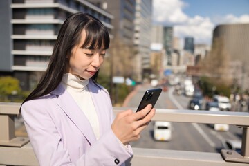 A portrait of Japanese woman using smartphone behind cherry blossom