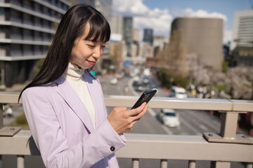A portrait of Japanese woman using smartphone behind cherry blossom