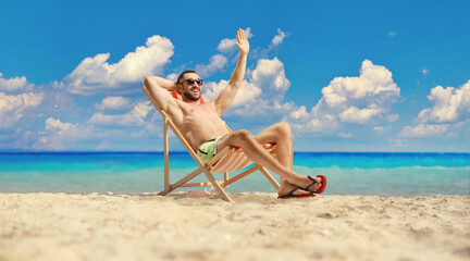 Young man in swimwear sitting on a beach chair and waving