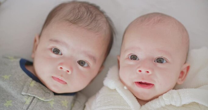 Cute little newborn twins boy and girl lie in bed smiling happily. Two caucasian babies brother and sister lying together in the bedroom at home. Happy family childhood positive kid bedtime lifestyle.