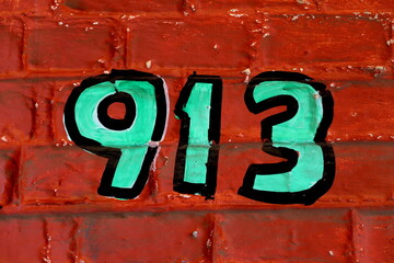 Numéro 913. Numéro de rue peint sur mur de brique rouge.