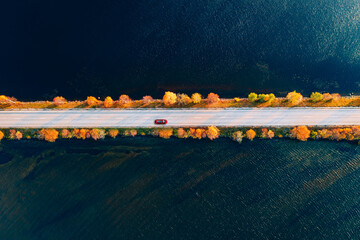 Aerial view of fall road and blue water lake sea ocean. Red car with a roof rack on a country road...