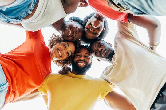 Close up portrait of young happy friends standing in circle and looking at camera - Millenial black african and latin people taking selfie - Lifestyle concept with guys and girls hugging together