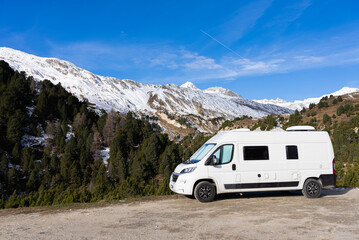 Obraz na płótnie Canvas 6m long white camper van in the mountains. The Camper is parked in an unpaved square and you can see the left side. The VanLife in the mountains in Switzerland.
