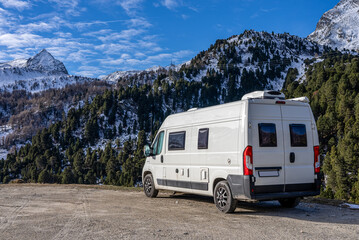 6m long white camper van in the mountains. The Camper is parked in an unpaved square and you can see the left side. The VanLife in the mountains in Switzerland. - Powered by Adobe