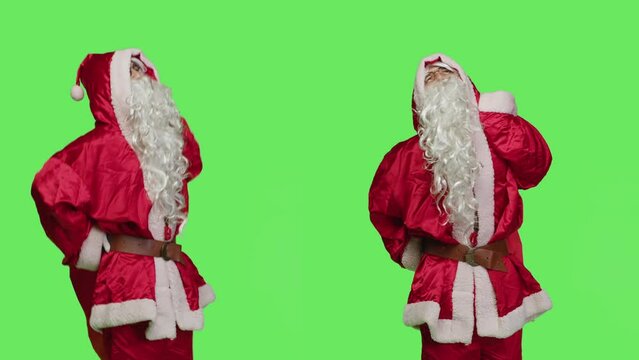 Ill man in festive suit having back pain, feeling sick while he is walking with red bag full of toys against greenscreen. Saint nick character being unwell with spinal ache, winter holiday concept.