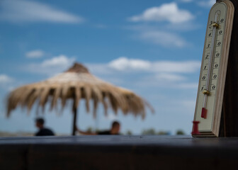 Termometr wskazujący wysoką temperaturę na plaży z parasolami z trzciny. - obrazy, fototapety, plakaty