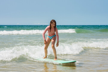 Pretty young girl sliding on ocean waves with her surfboard