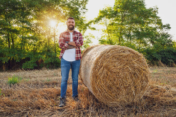 Naklejka na ściany i meble Farmer is standing beside bales of hay. He is satisfied after successful harvesting.