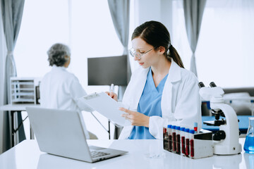 Obraz na płótnie Canvas Two scientist or medical technician working, having a medical discuss meeting with an Asian senior female scientist supervisor in the laboratory with online reading, test samples and innovation