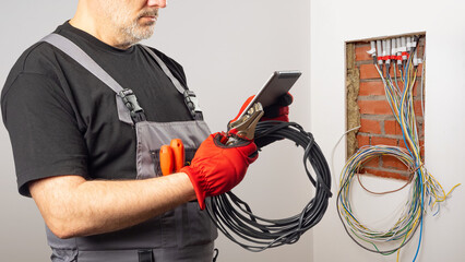 Man electrician. Worker with wires and tablet. Installation wiring in room. Cropped electrician...