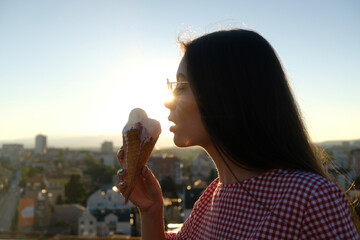 Woman licking melting ice cream at sunset in the city in summer