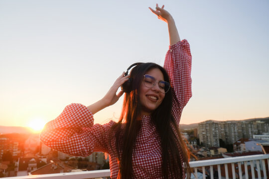 Young woman smiling and listening to music on headphones in the city at sunset. 