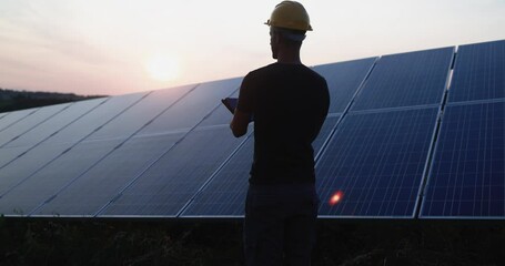 Young engineer working at solar power station outdoor while using digital tablet - Renewable green energy and environmental concept