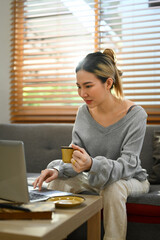 Pleasant young woman communicating in social network, searching information online on laptop at home