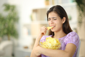 Sad woman eating chips at home