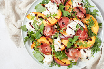 Healthy summer salad with peach, burrata, arugula and jamon