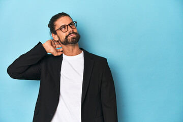 Businessman in suit with eyeglasses and beard touching back of head, thinking and making a choice.