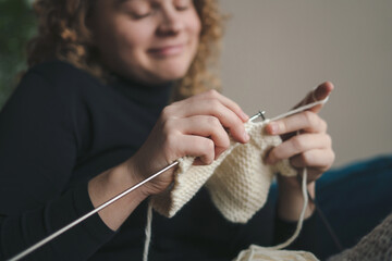 Close-up view of a woman's hands knitting in cozy light. Crochet thick threads. Home comfort.