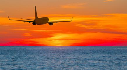 Airplane in the sky flying over tropical sea at sunset