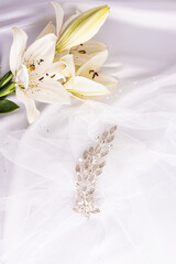 Obraz na płótnie Canvas Beautiful vertical wedding background. A gorgeous comb with rhinestones on the bride's snow-white veil and white live lilies. decor. layout