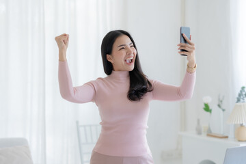 Fototapeta na wymiar Happy young Asian woman raising hands with victory smiling happily with smart phone at home. Success, win, victory, triumph, congratulation, concept.