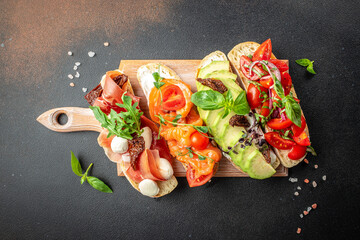 a set of bruschetta with prosciutto, salmon, tomatoes and avocado on a wooden board, banner, menu,...