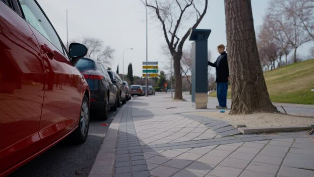 Sidewalk pavement with blurred confident woman walking to parking meter paying. Blond Caucasian female driver using parking machine in urban city outdoors