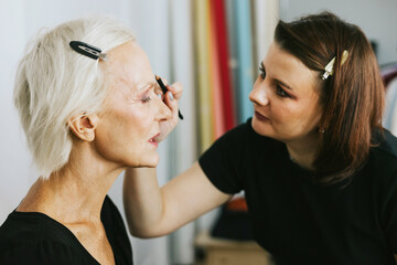 makeup for an age model, a girl does makeup in the studio for a beautiful adult elderly woman