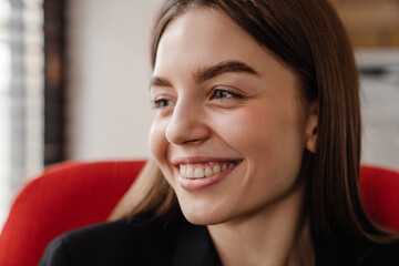 Young woman smiling and looking away while sitting on armchair indoors