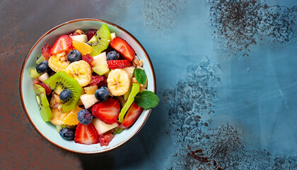 Bowl of healthy fresh fruit salad on a blue rusty background. Top view with copy space. Flat lay