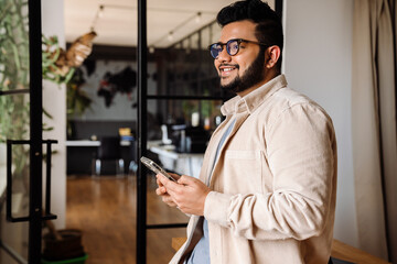 Young indian business man using smartphone while standing in office