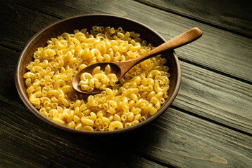 Vintage plate with raw pasta and spoon on the kitchen table before preparing dinner. Place for a recipe or menu on a black background