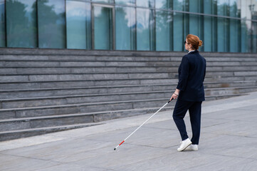 Blind business woman in glasses and with a cane climbs the stairs to the business center. 