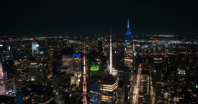Night Aerial Footage of New York City with Skyscraper Spires and Straight Busy Streets with Cars and Yellow Taxi Vehicles. Lowered Helicopter View of Office Buildings in a Big Urban Center