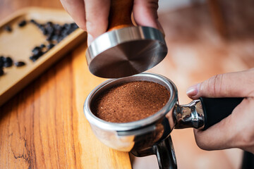 Close-up of hand Barista cafe making coffee with manual presses ground coffee using tamper on the wooden counter bar at the coffee shop